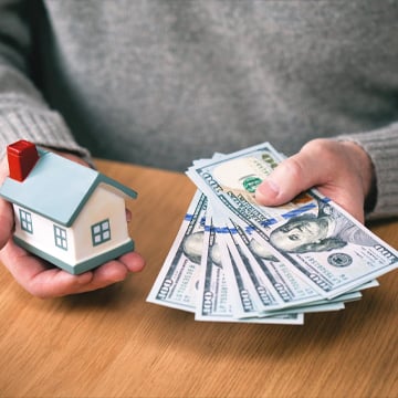 personne tenant une maison miniature et de l'argent