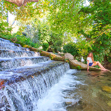 a lady sitting on the side of a small pond surrounded greenery a lady sitting on the side of a small pond surrounded greenery