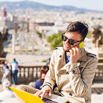 young guy in beige coat sitting on hight on city background with laptop and phone